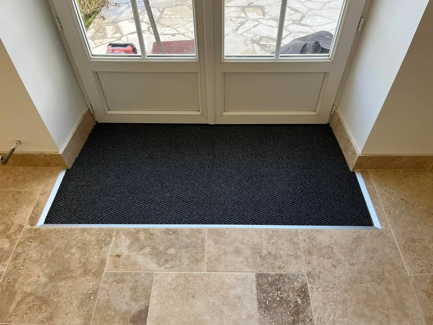 Entrée d'une habitation réalisée en jonction parfaite avec du travertin et le paillasson de la porte d'entrée incrusté